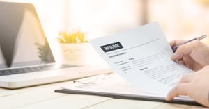 Hands holding resume on a desk with a laptop.
