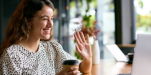 Young woman waves at computer for virtual networking event