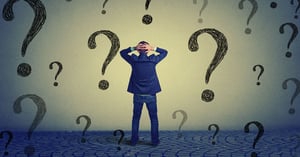 Man with hands on his head facing wall of question marks